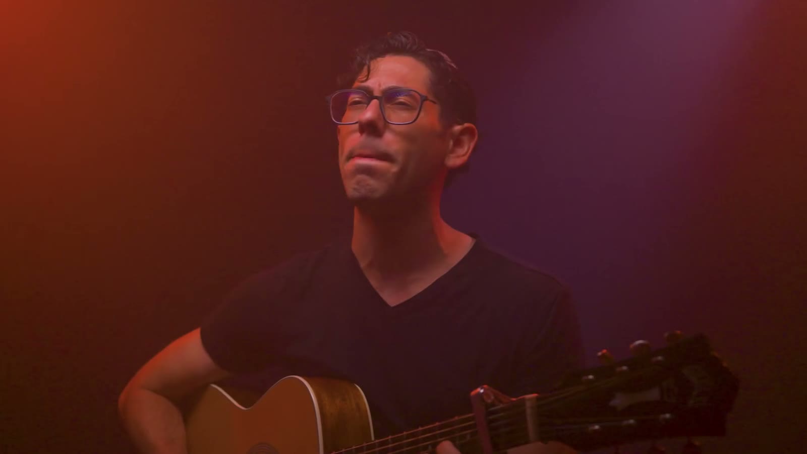 Shlomo Lipman singing with his guitar under red light, from Soldiers of Truth